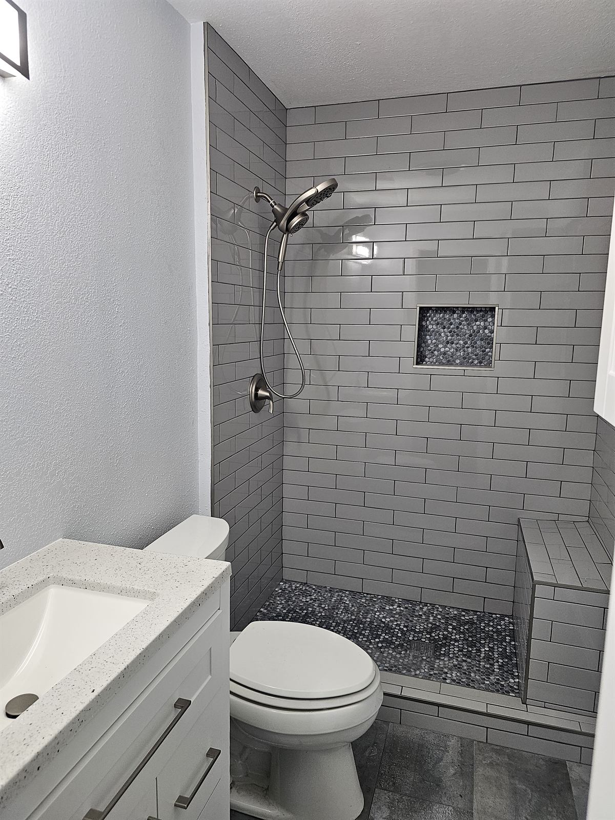Completed bathroom with subway-tiled shower, bench, and mosaic floor