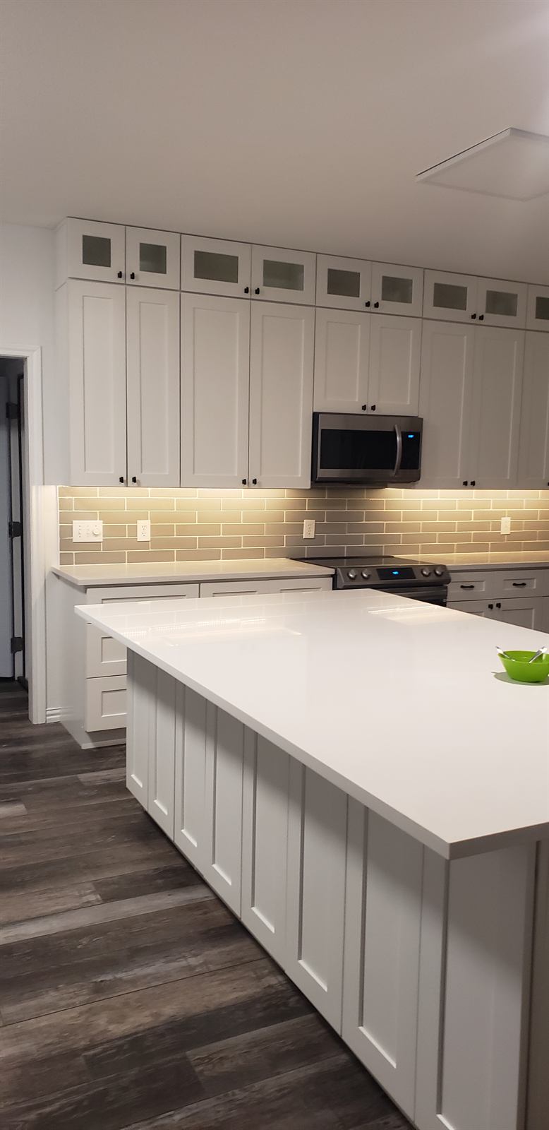 Remodeled kitchen with white cabinetry, a quartz island, and wood-look flooring