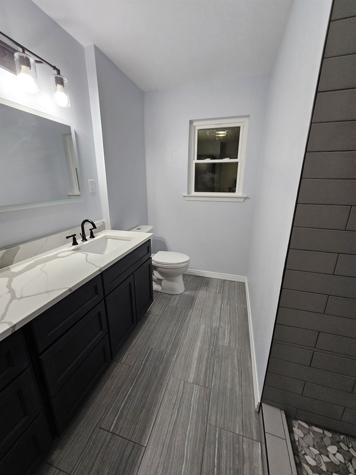 Completed bathroom with dark vanity, quartz top, and tiled walk-in shower